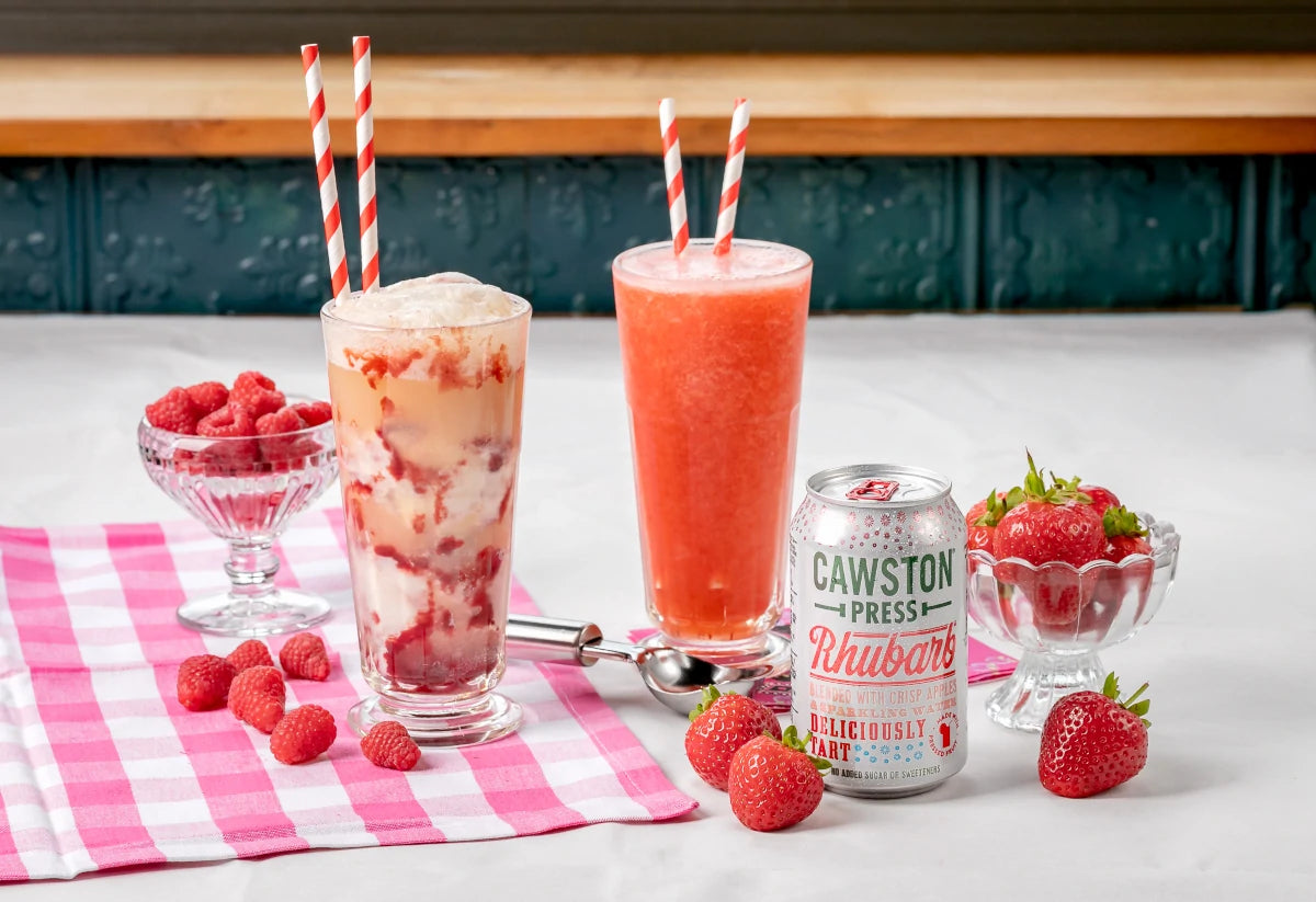 The two soda floats on a table with a Cawston can and fresh fruit