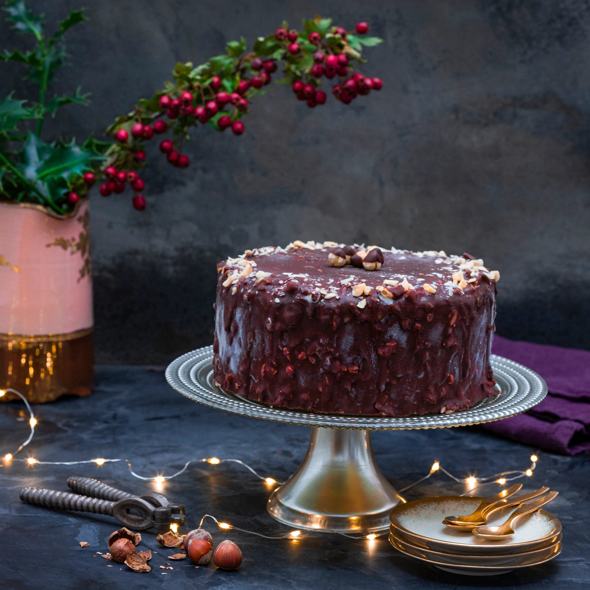 An ice cream cake coated in dark chocolate, and decorated with hazelnuts, against a festive background.