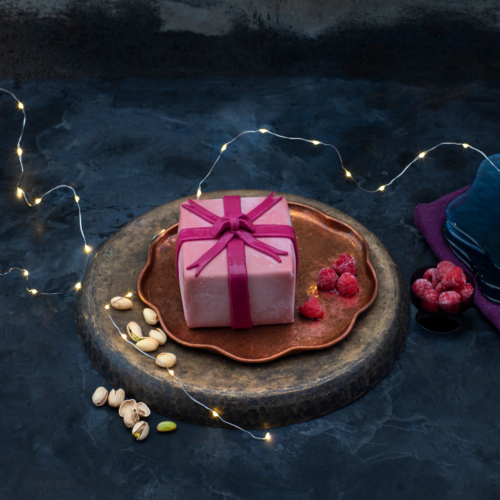 A desserts shaped like a gift, coated in pink chocolate with a bow.