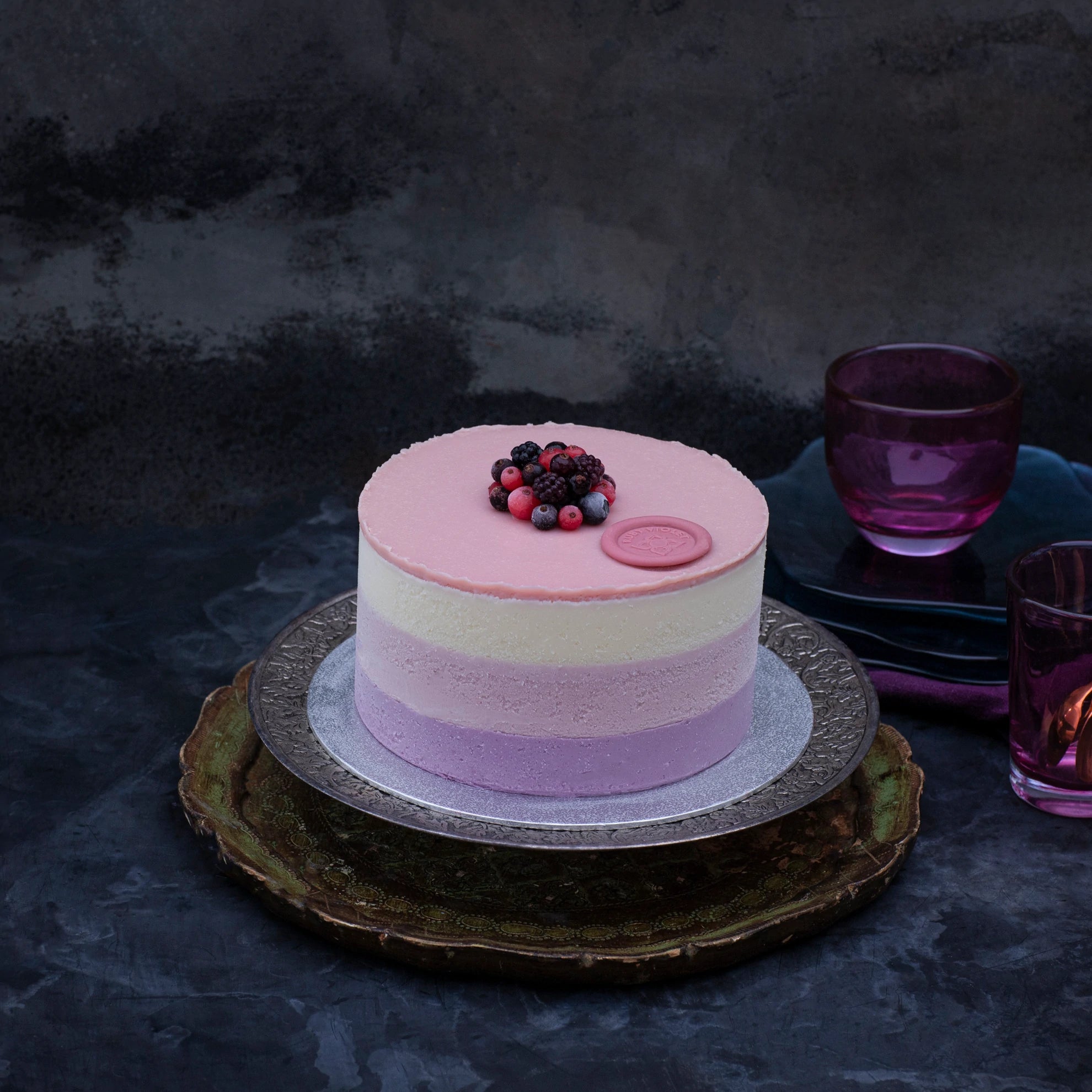 Miss Elodie ice cream cake, a white, pink and purple cake with a pink ganache top, on a tray, decorated with frozen fruit.