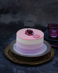 Miss Elodie ice cream cake, a white, pink and purple cake with a pink ganache top, on a tray, decorated with frozen fruit.