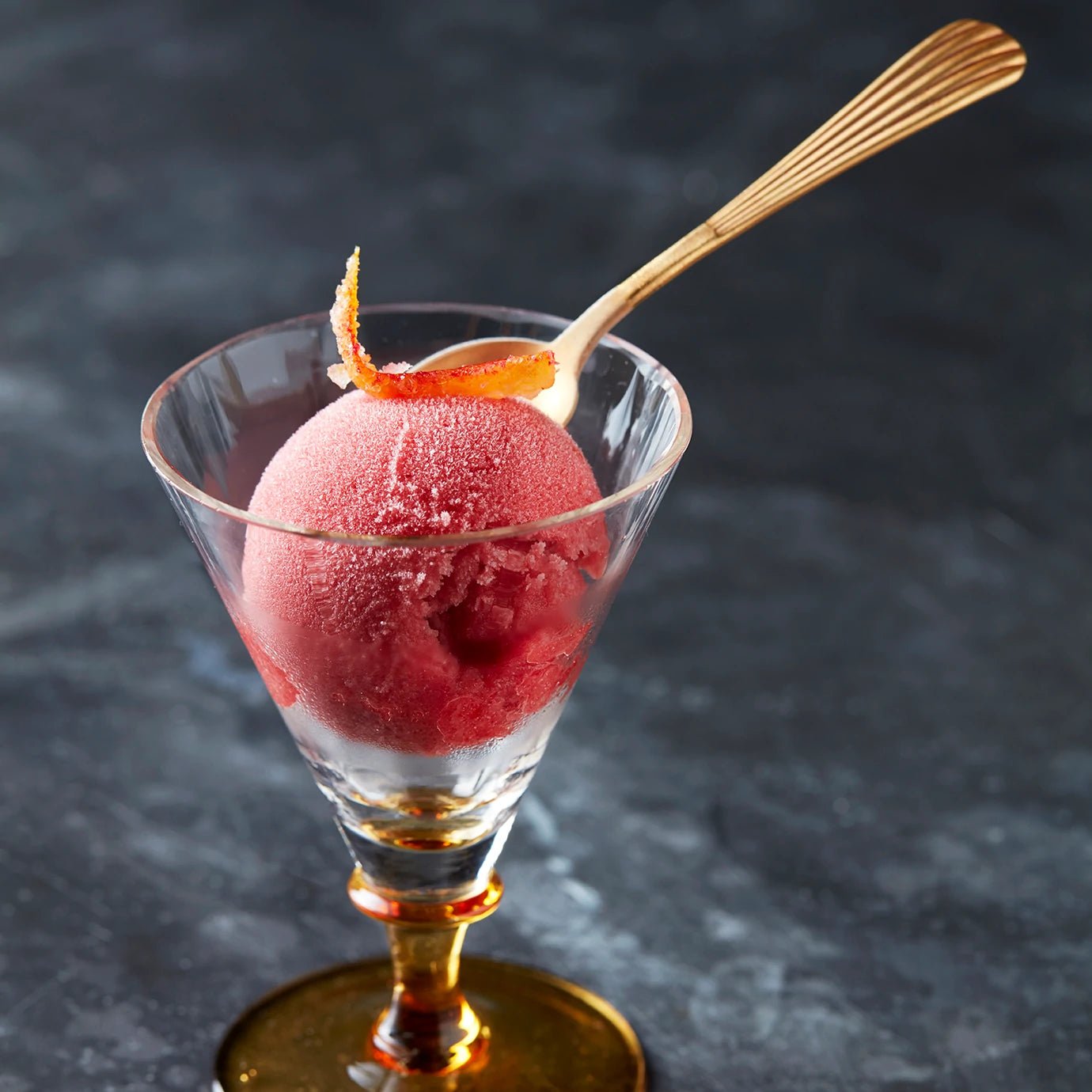 Scoop of Blood Orange & Campari sorbet in a glass with a golden spoon