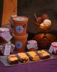 Ice cream tubs, scoops of ice cream, jars of sauce and 4 golden ice cream bullion bars on a purple surface.