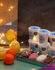Frozen lemons and clementines, 6 little ice cream tubs piled on each other and 4 colourful ice creams on stick surrounded by fairy lights.