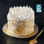 A white cake topped with meringues and decorated with gold foil, set against a black background.