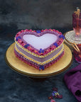 A purple heart shaped cake decorated with colourful ganache piping and violets, against a dark background.