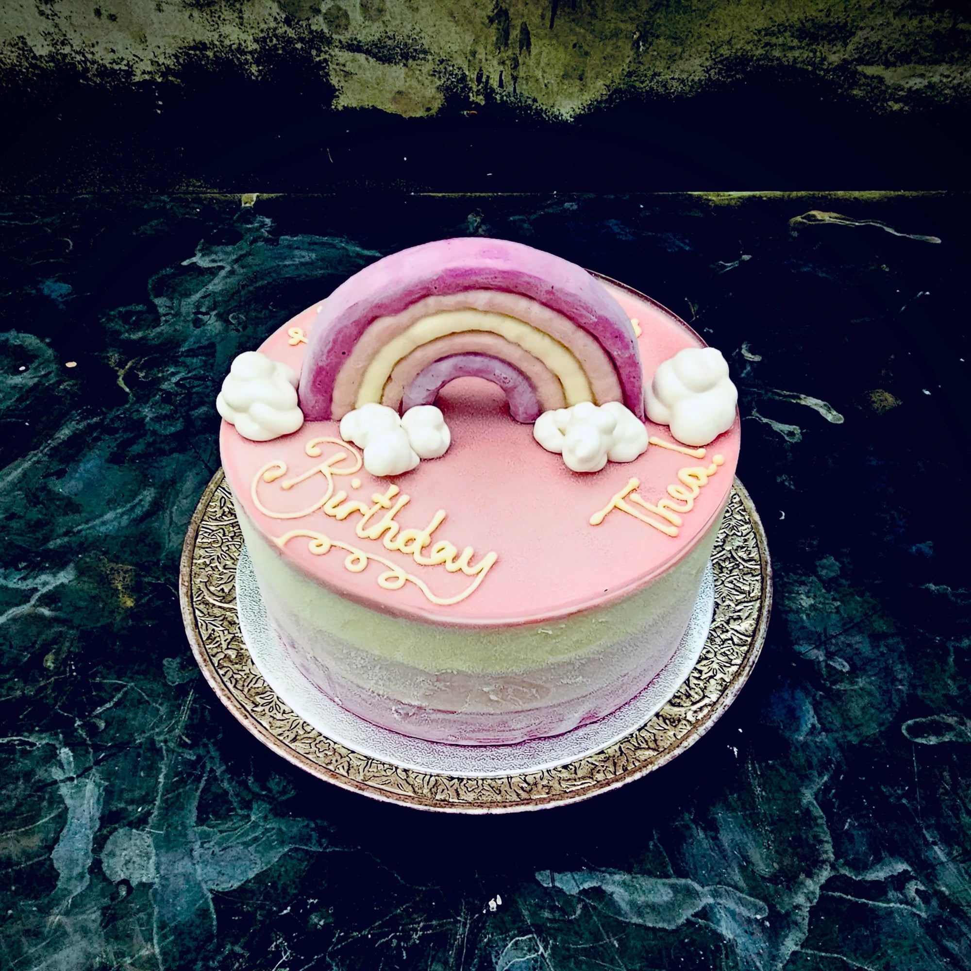 Bespoke ice cream cake topped with pink ganache, decorated with a rainbow and clouds topper.