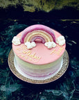 Bespoke ice cream cake topped with pink ganache, decorated with a rainbow and clouds topper.