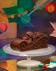 An ice cream cake coated in dark chocolate, shaped like Santa on his sleigh, on a stand against a festive background.