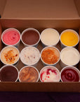 Assorted ice cream flavors in small tubs inside a cardboard box on a dark background