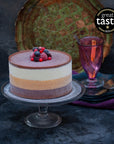 An ice cream cake with white, orange and brown layers, topped with frozen berries, on a stand against a dark background.