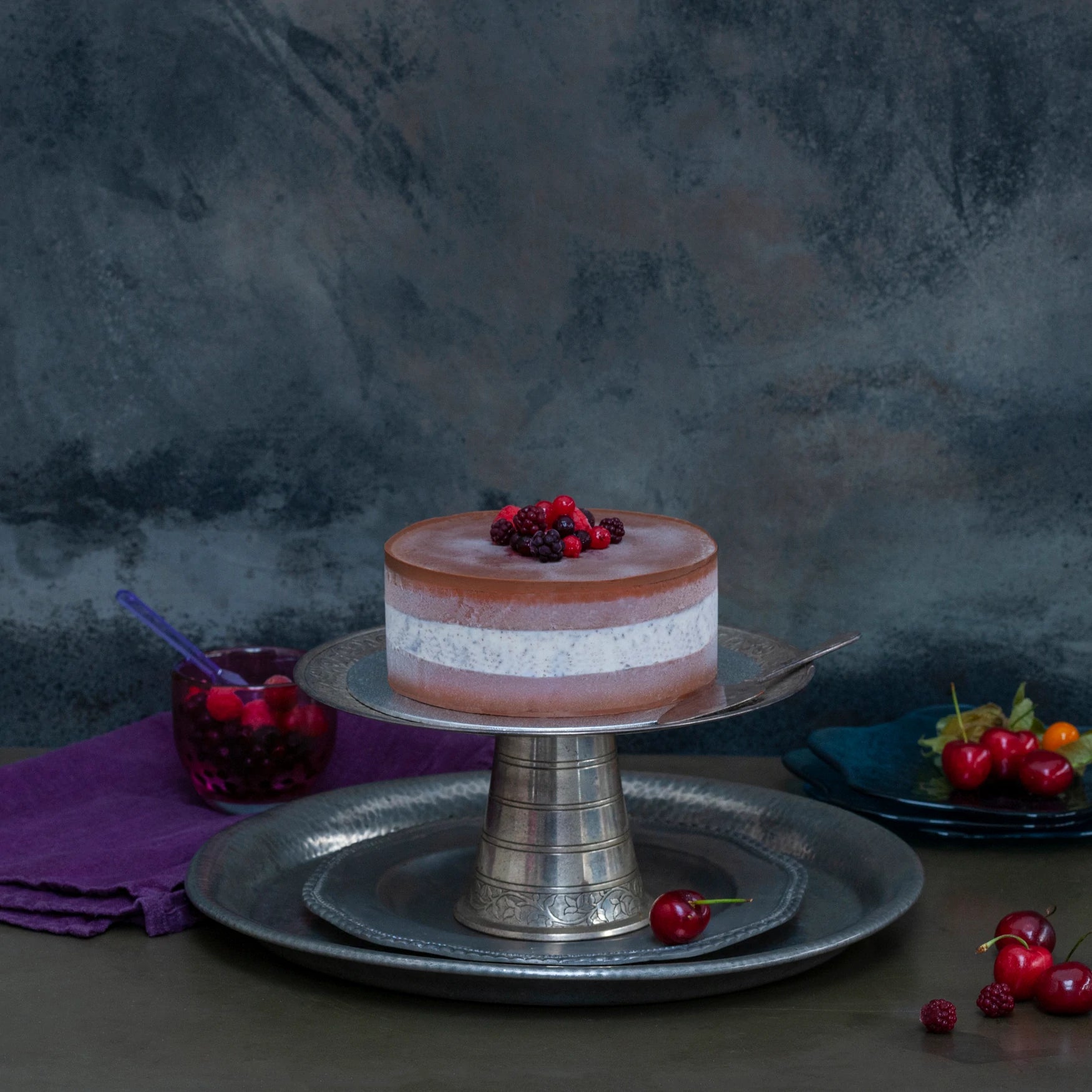 A white and brown ice cream cake on a silver stand, decorated with frozen berries.