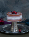 A white and brown ice cream cake on a silver stand, decorated with frozen berries.
