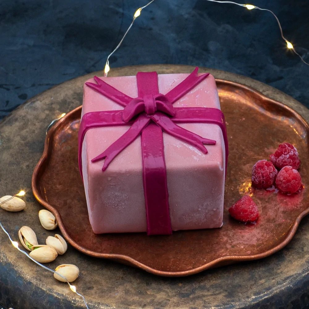 A desserts shaped like a gift, coated in pink chocolate with a bow.