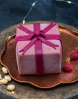 A desserts shaped like a gift, coated in pink chocolate with a bow.