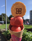 Two scoops of strawberry sorbet in a cone with a wafer
