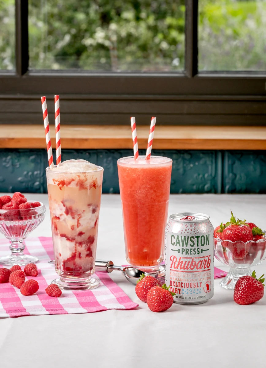 The two soda floats on a table with a Cawston can and fresh fruit