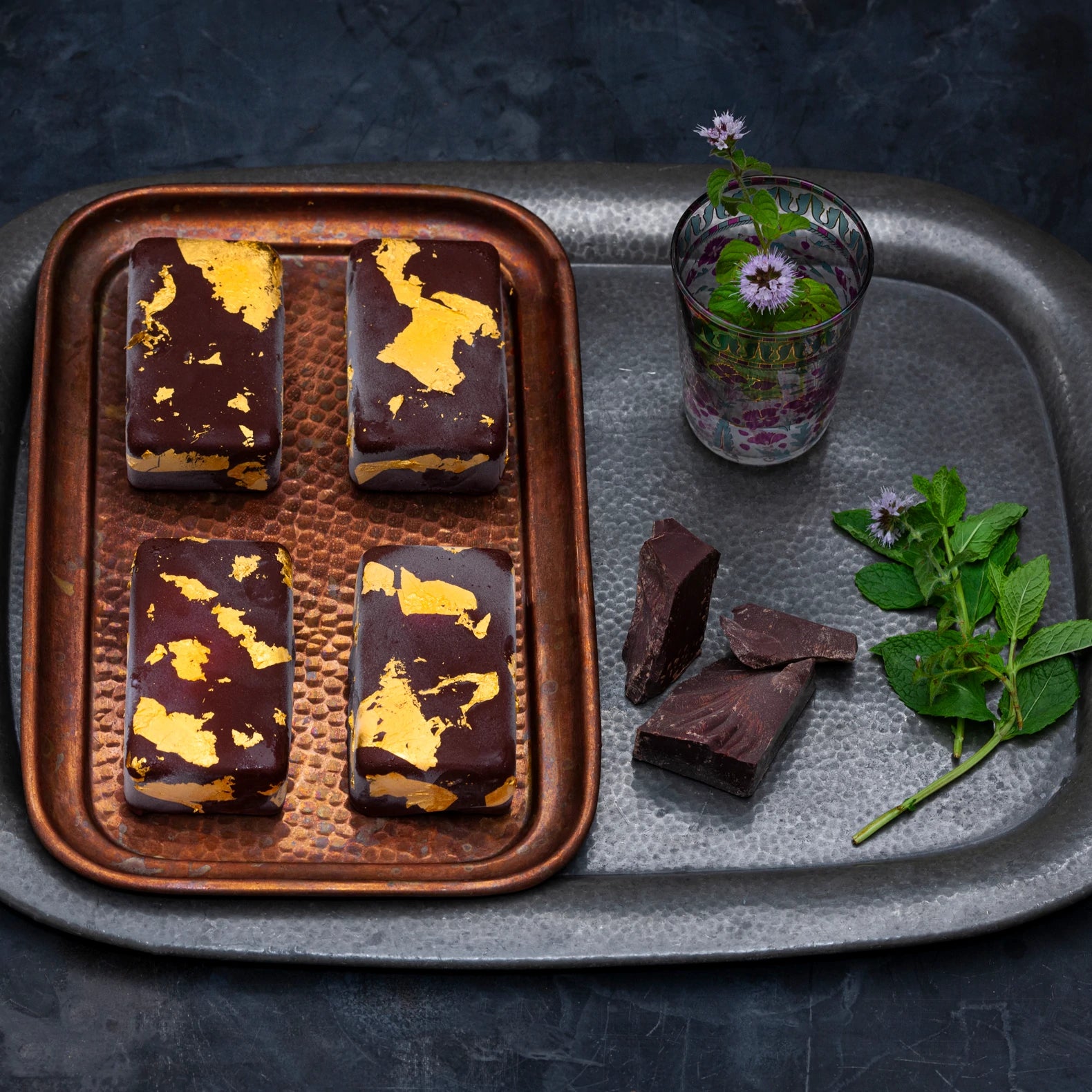 Four gold mint chocolate bars on a tray with fresh mint and dark chocolate