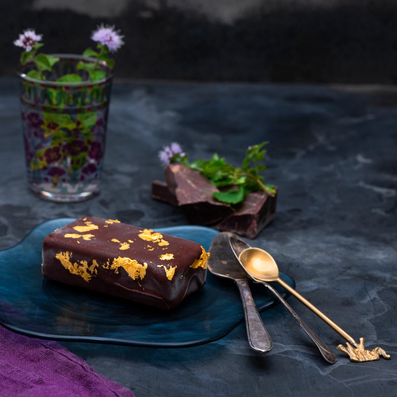 A gold mint chocolate bar on a tray with fresh mint and dark chocolate