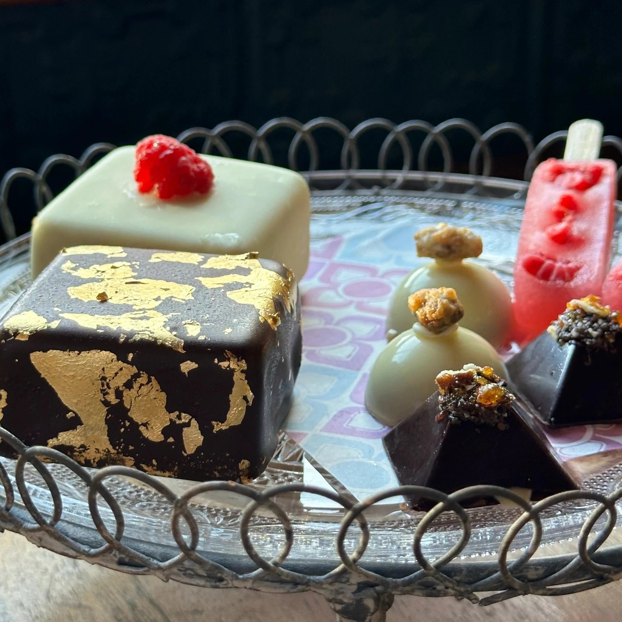 Square ice cream cakes coated in chocolate next to 4 ice cream chocolates and a sorbet on a stick