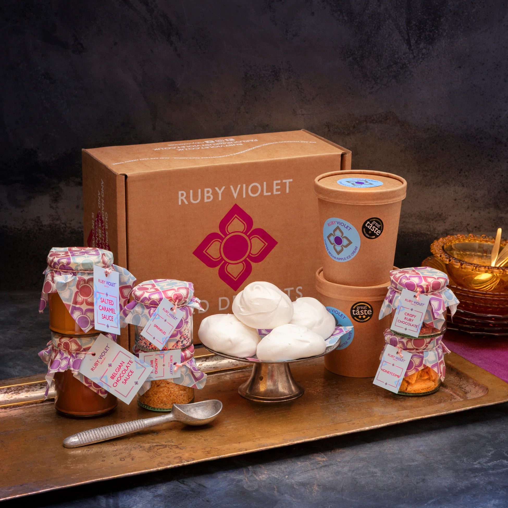 A cardboard gift box with ice cream tubs, meringues and colourful glass jars on a vintage ray, against a dark background. 