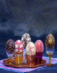 Six easter eggs filled with ice cream and decorated with different motifs sitting in coloured glass cups.