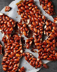 A close-up of almond nut brittle topping with visible almonds and a dark, textured background.