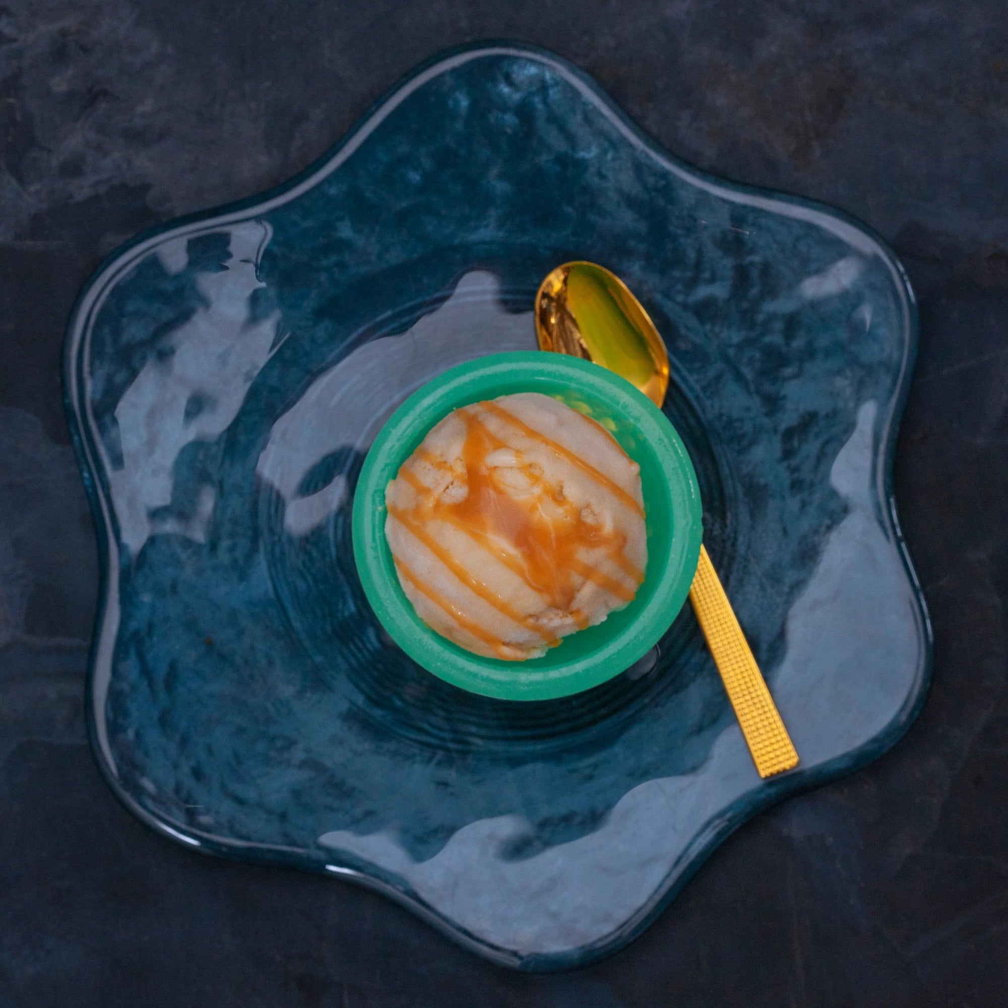 Scoop of banana caramel ice cream on a blue plate with a golden spoon