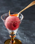 Scoop of Blood Orange & Campari sorbet in a glass with a golden spoon