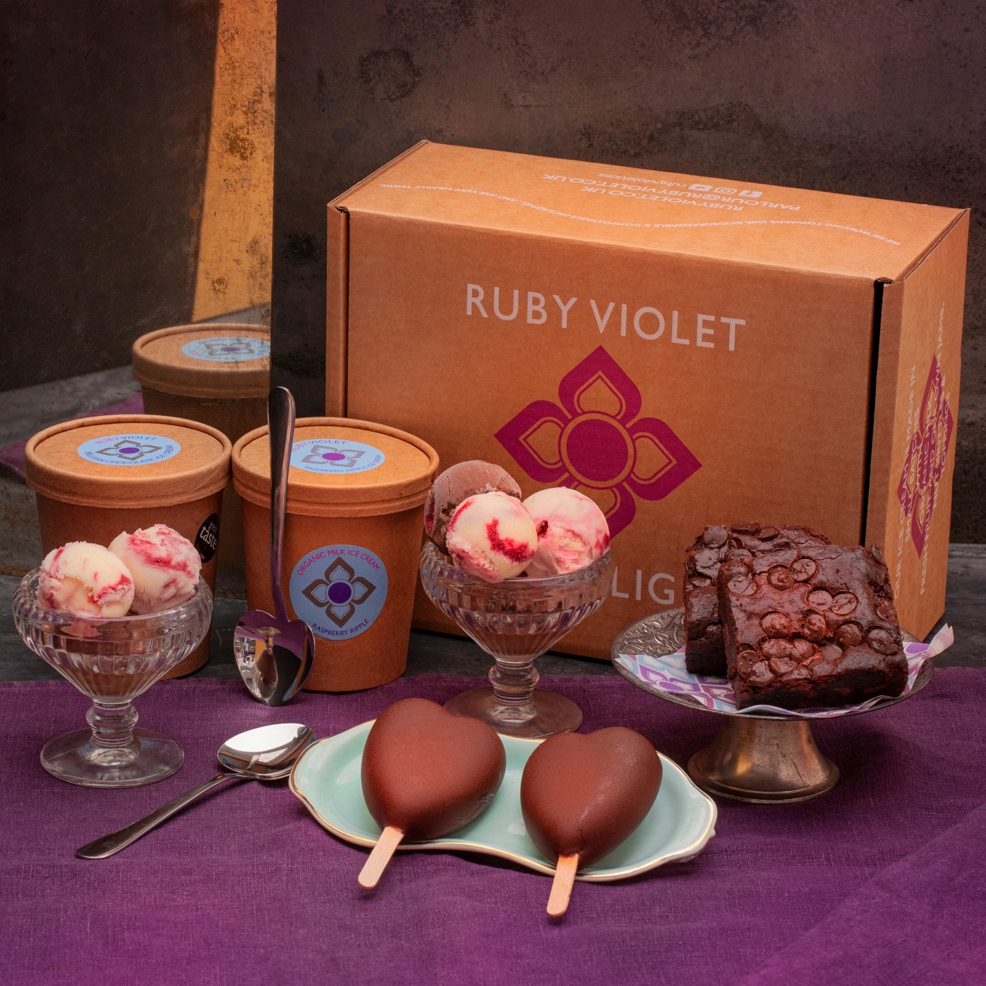 Ice cream products and brownies in front of a Ruby Violet gift box, set on a purple tablecloth.