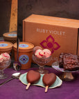 Ice cream products and brownies in front of a Ruby Violet gift box, set on a purple tablecloth.