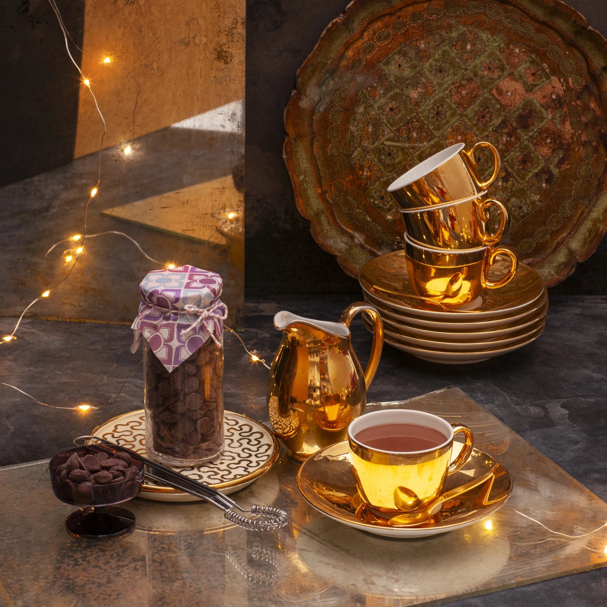 Hot chocolate in a golden cup, next to a glass jar full of chocolate callets