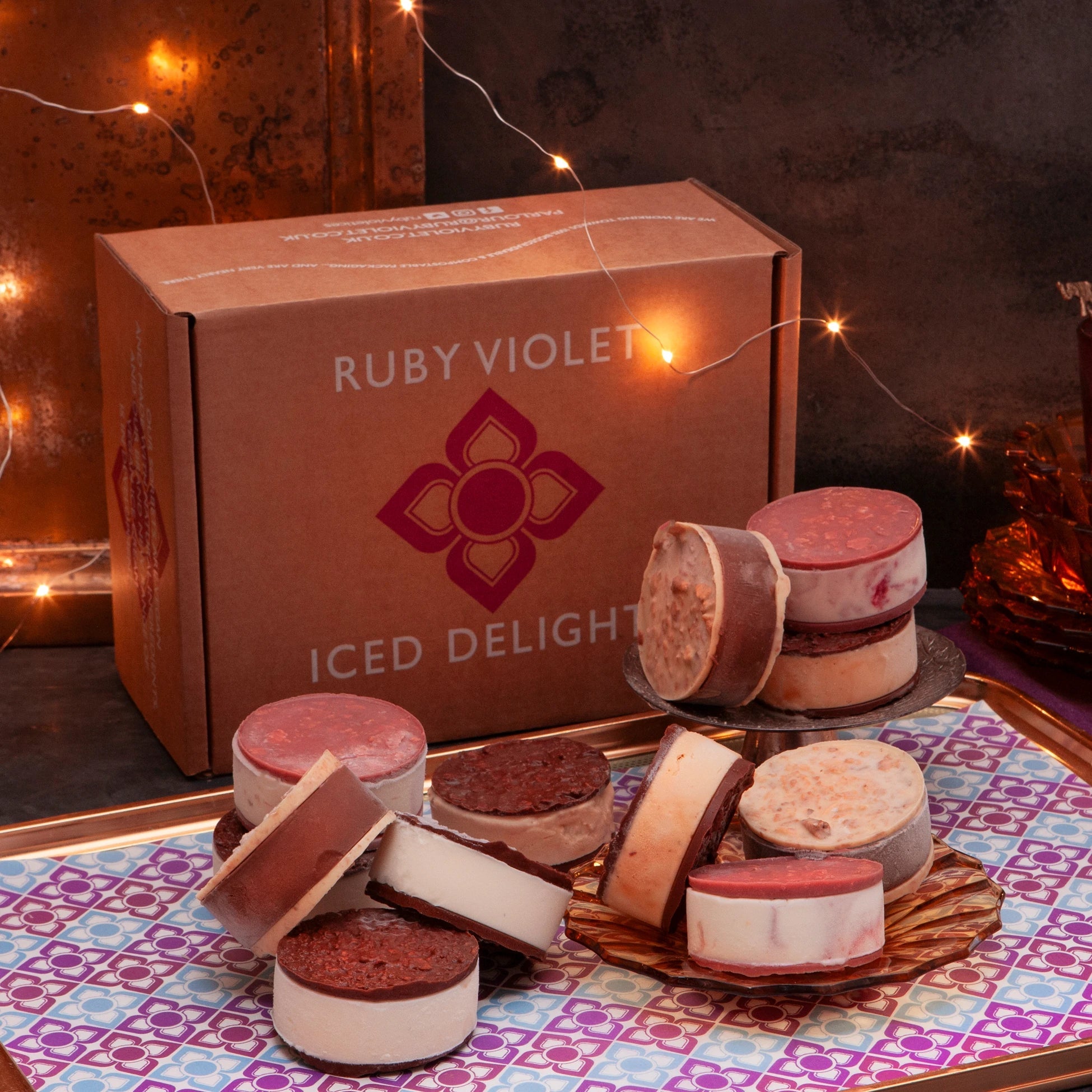 Ice cream sandwiches in different flavours on a tray, in front of a Ruby Violet box on a  table with string lights in the background