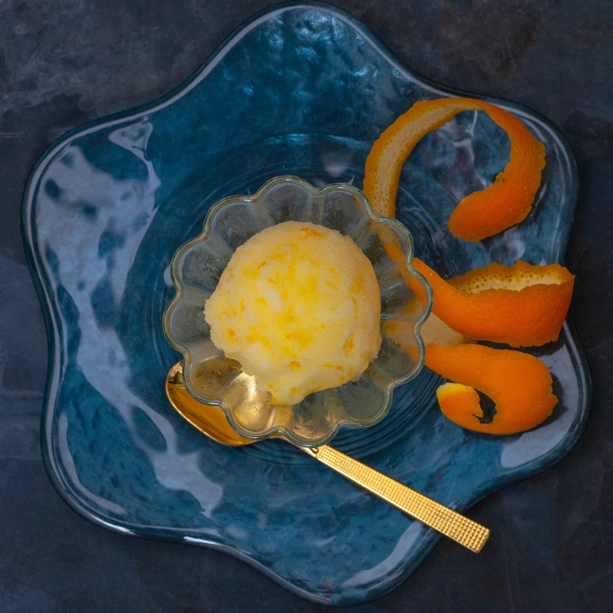 A scoop of orange sorbet with a golden spoon and orange peel