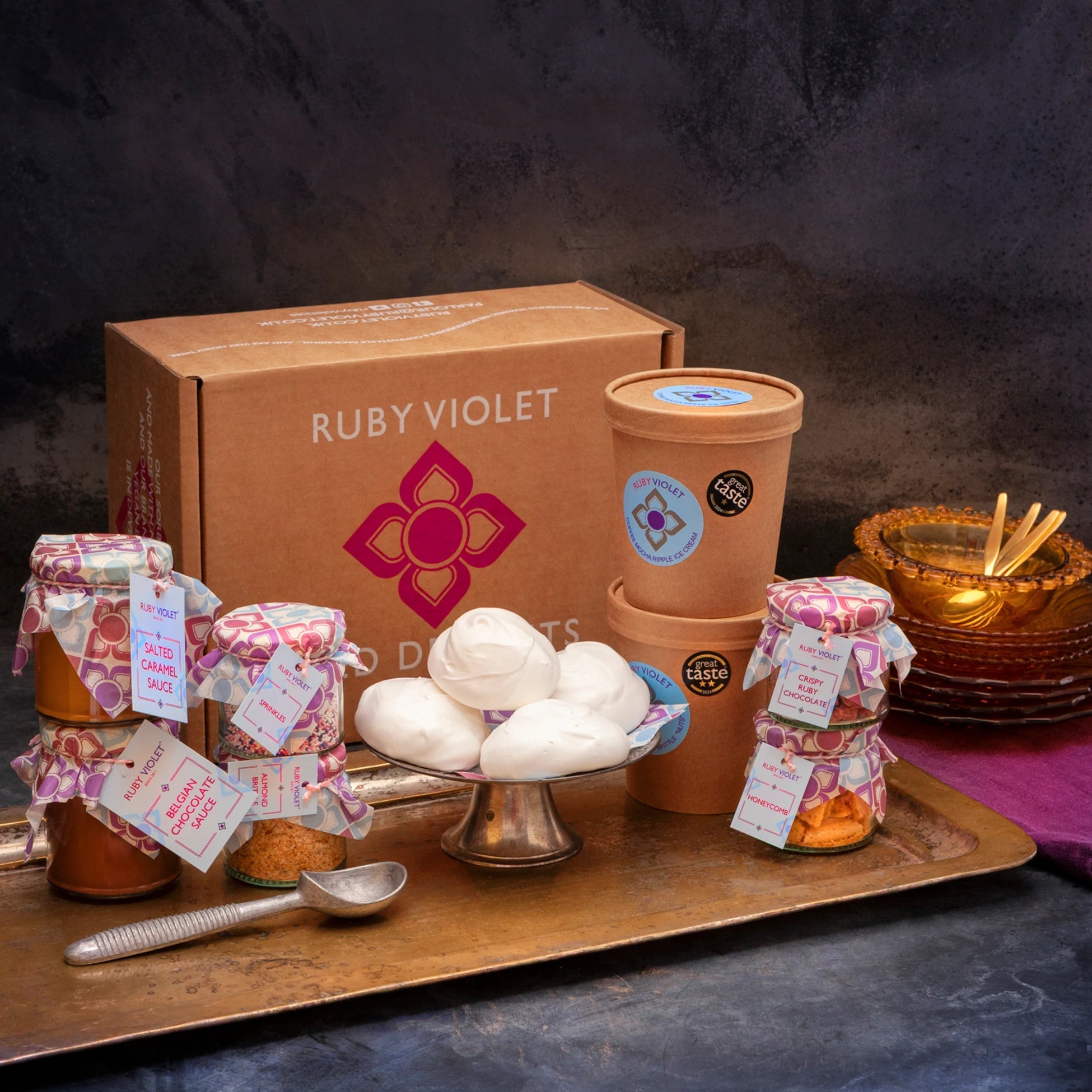 A cardboard gift box with ice cream tubs, meringues and colourful glass jars on a vintage ray, against a dark background. 