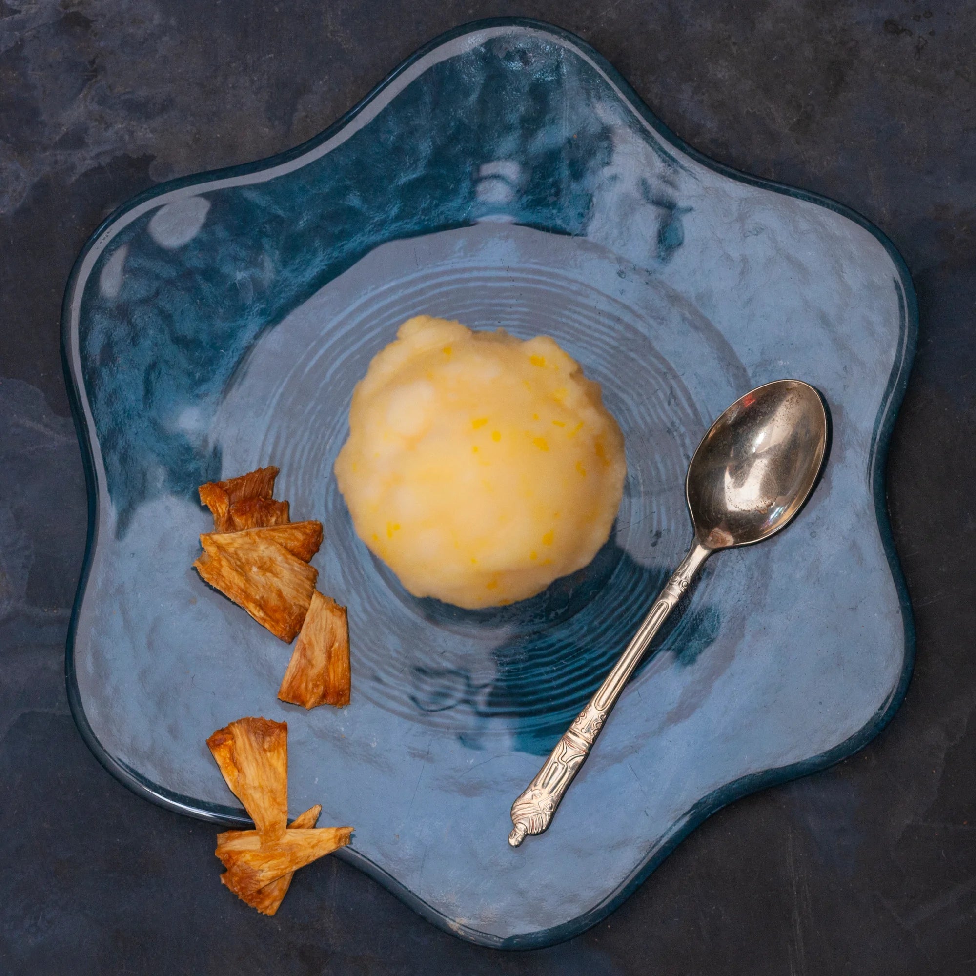 A scoop f pineapple sorbet on a plate with pieces of desiccated pineapple 