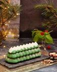 Christmas tree shaped dessert on a dark surface with festive decorations in the background
