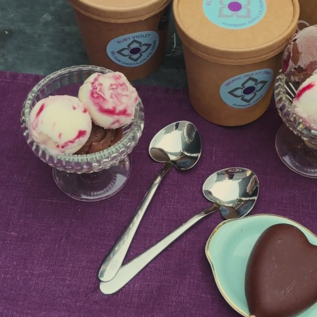 A video that pans over ice cream scoops in glass bowls, heart shaped teaspoons, 2 heart shaped ice creams on sticks coated in milk chocolate and 2 chocolate brownies on a plate