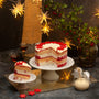 A tall Xmas cake with different coloured layers, topped with white ganache and red flowers, on a festive background.