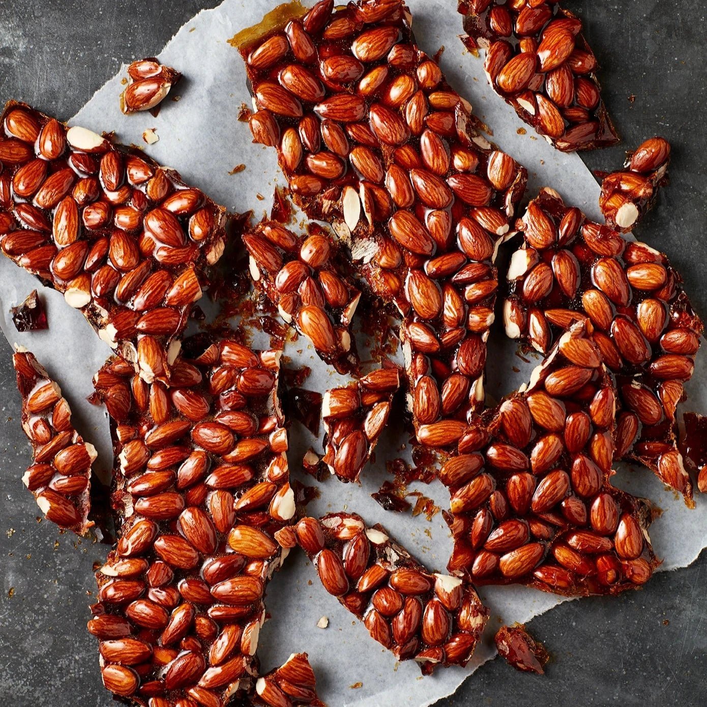 A close-up of almond nut brittle topping with visible almonds and a dark, textured background.