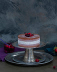 A white and brown ice cream cake on a silver stand, decorated with frozen berries.