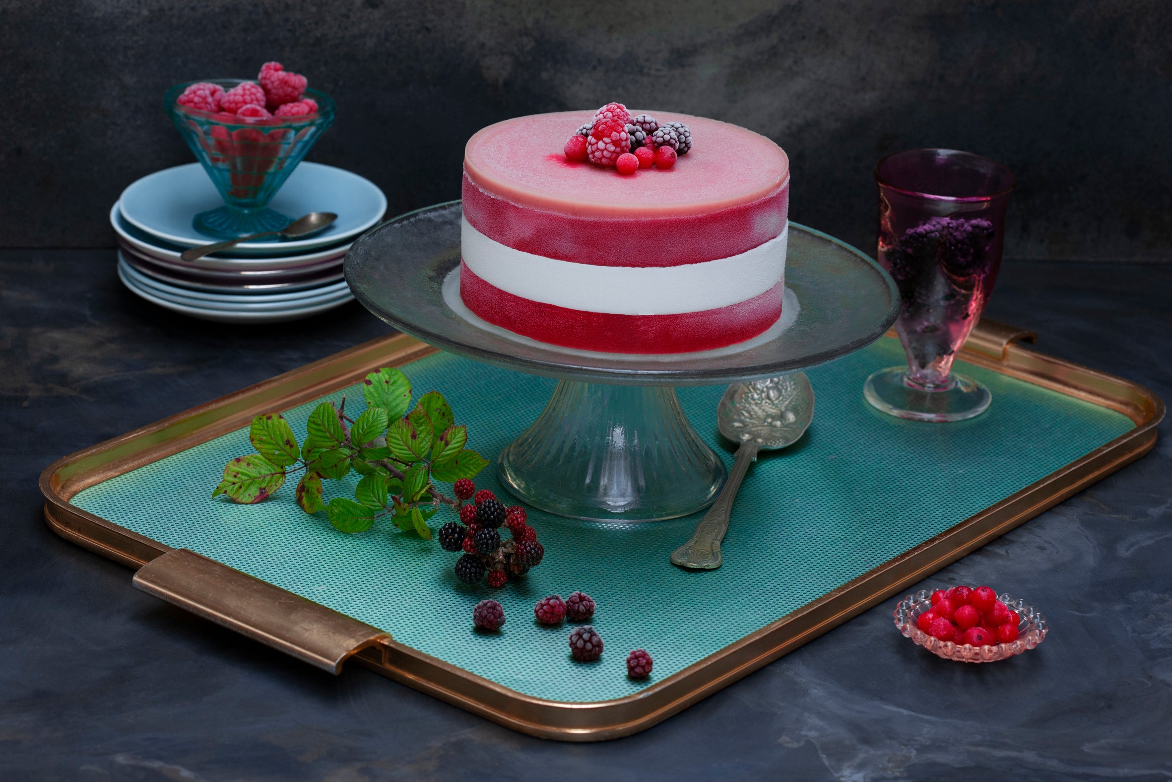 Handmade vegan rasoberry and coconut cake on a tray, styled with frozen fruits